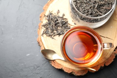 Photo of Aromatic black tea in cup and dry leaves on grey table, top view. Space for text