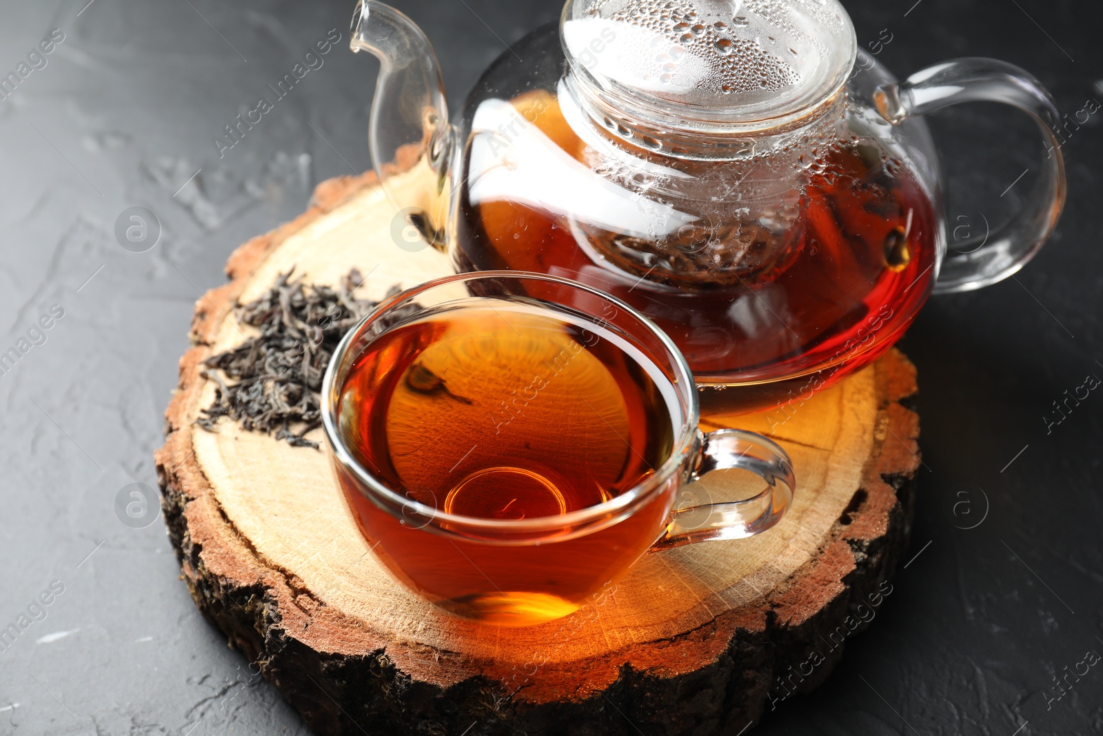 Photo of Aromatic black tea and dry leaves on grey table, closeup