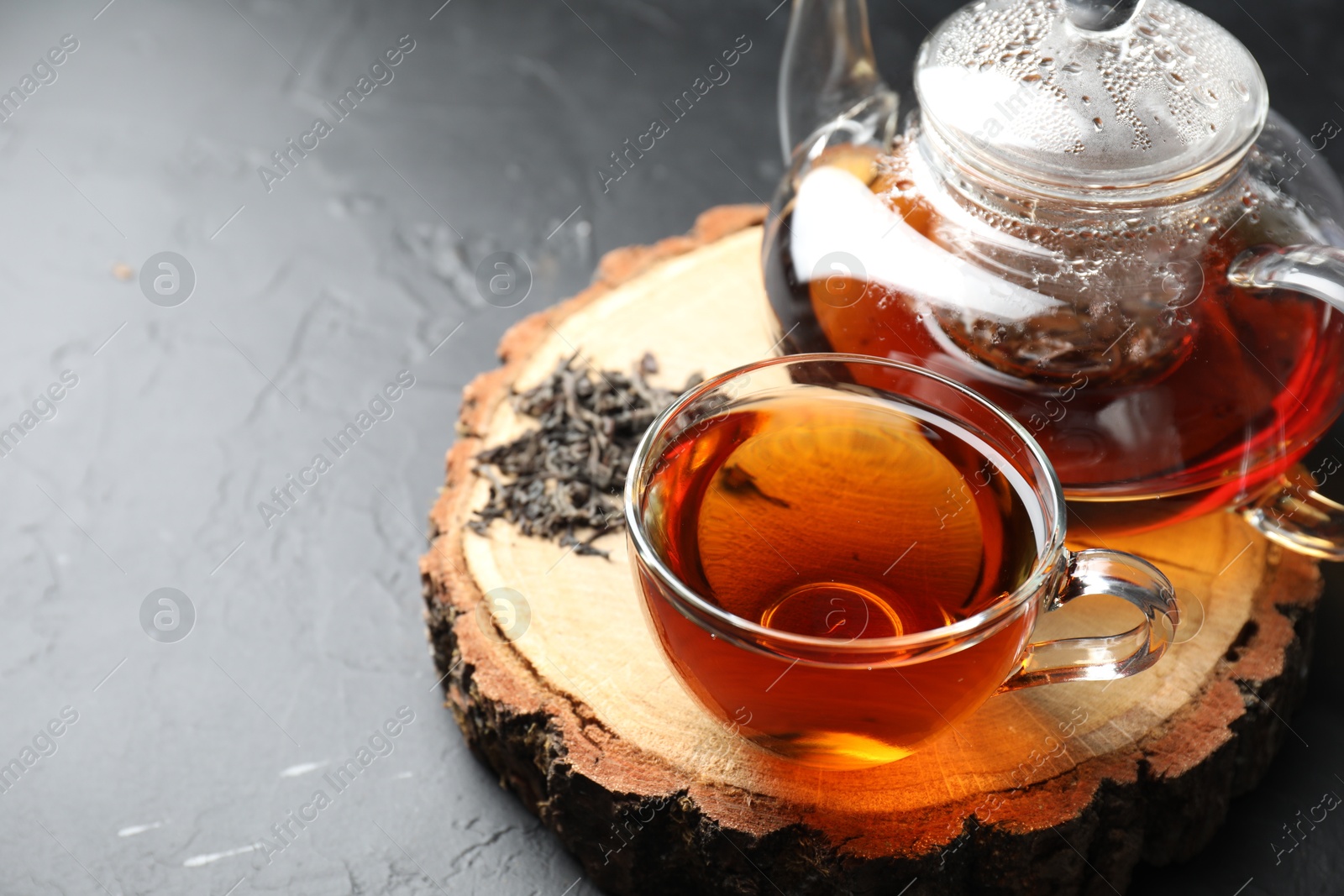 Photo of Aromatic black tea and dry leaves on grey table, closeup. Space for text