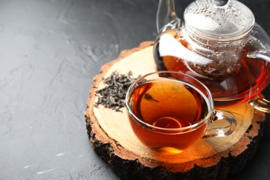 Photo of Aromatic black tea and dry leaves on grey table, closeup. Space for text