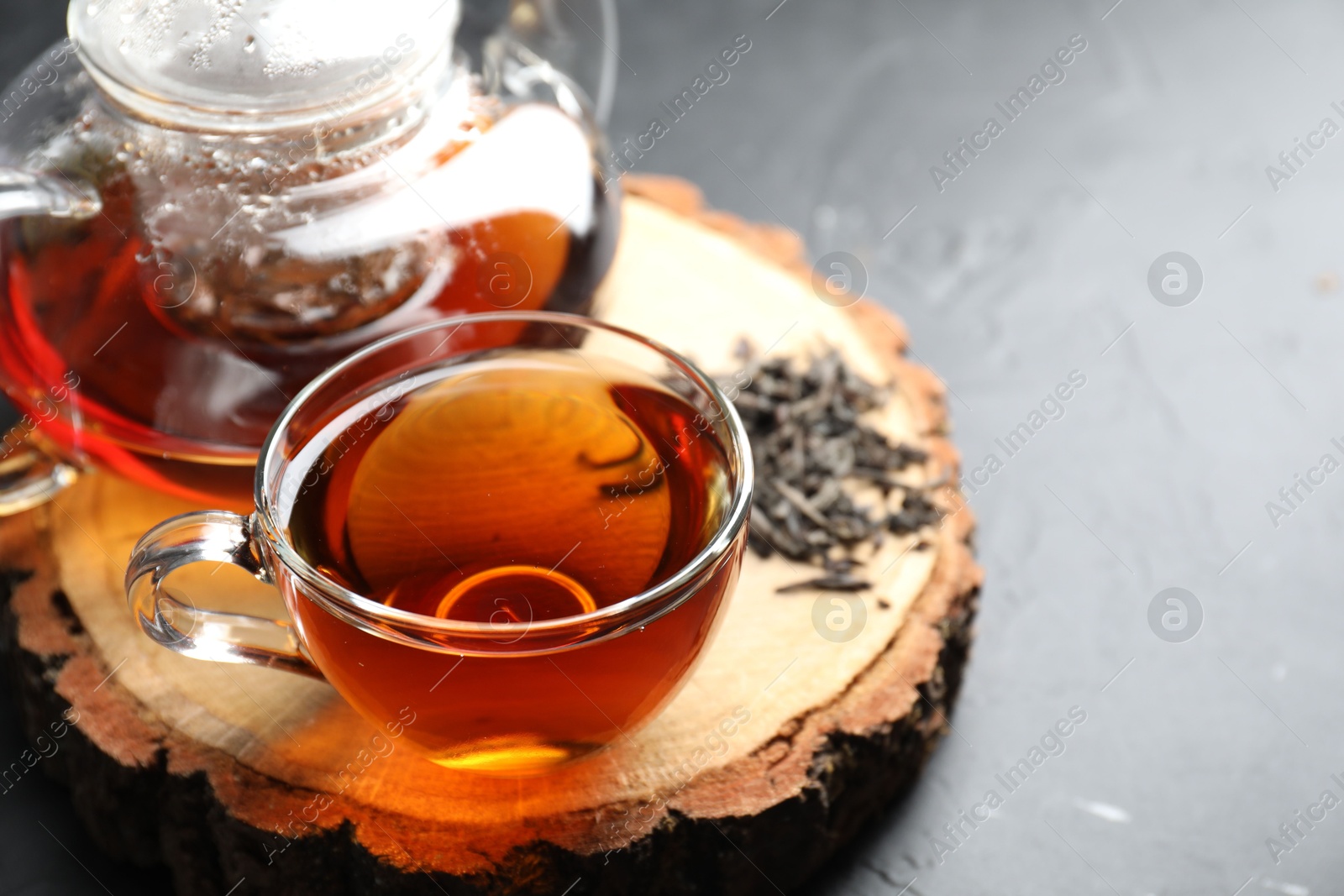 Photo of Aromatic black tea and dry leaves on grey table, closeup. Space for text