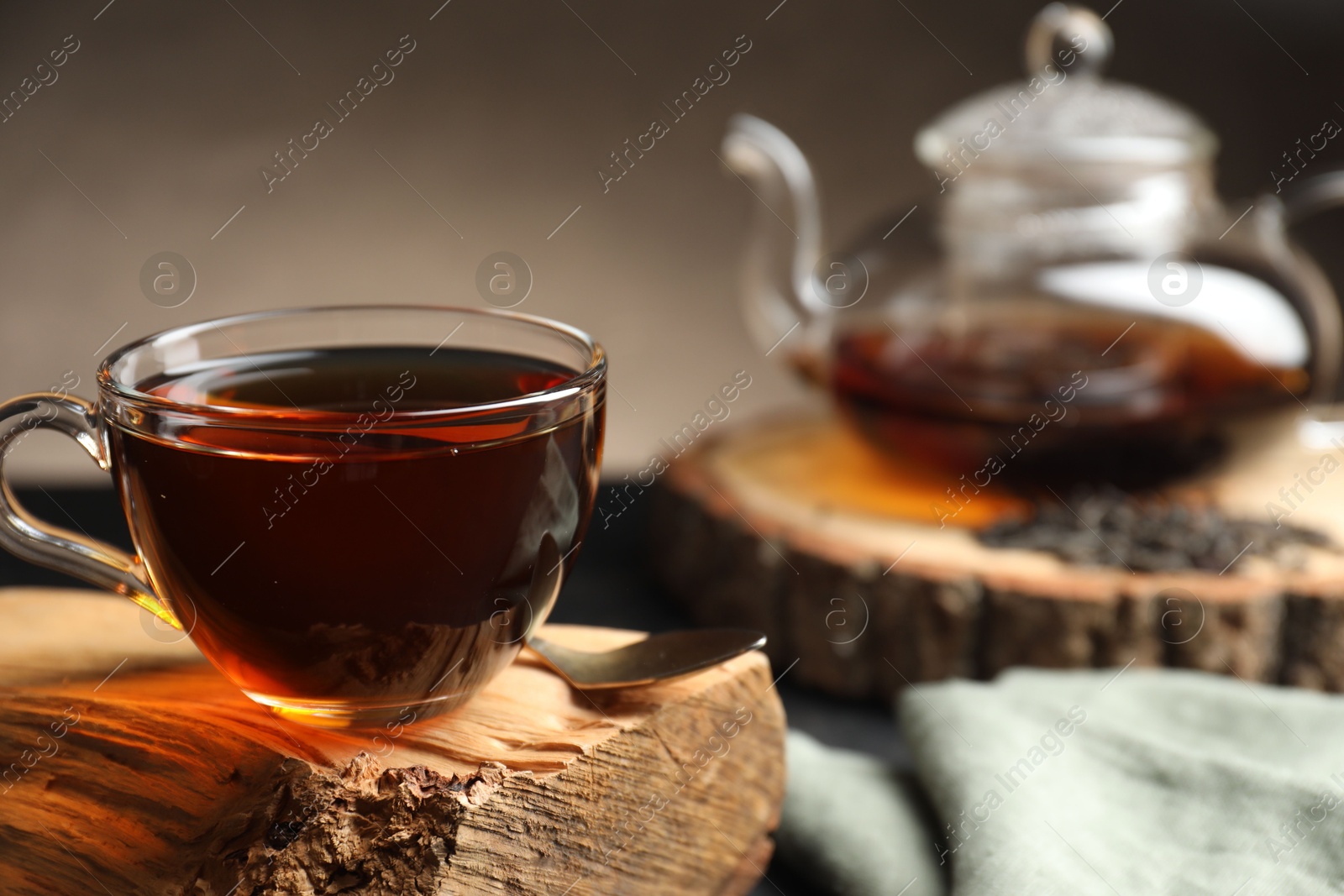 Photo of Aromatic black tea in cup on wooden snag, closeup