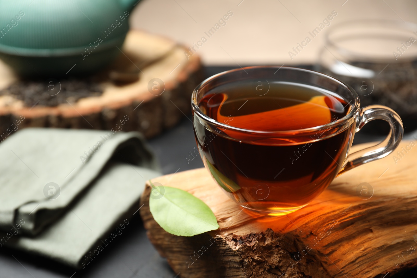 Photo of Aromatic black tea in cup and green leaf on table, closeup