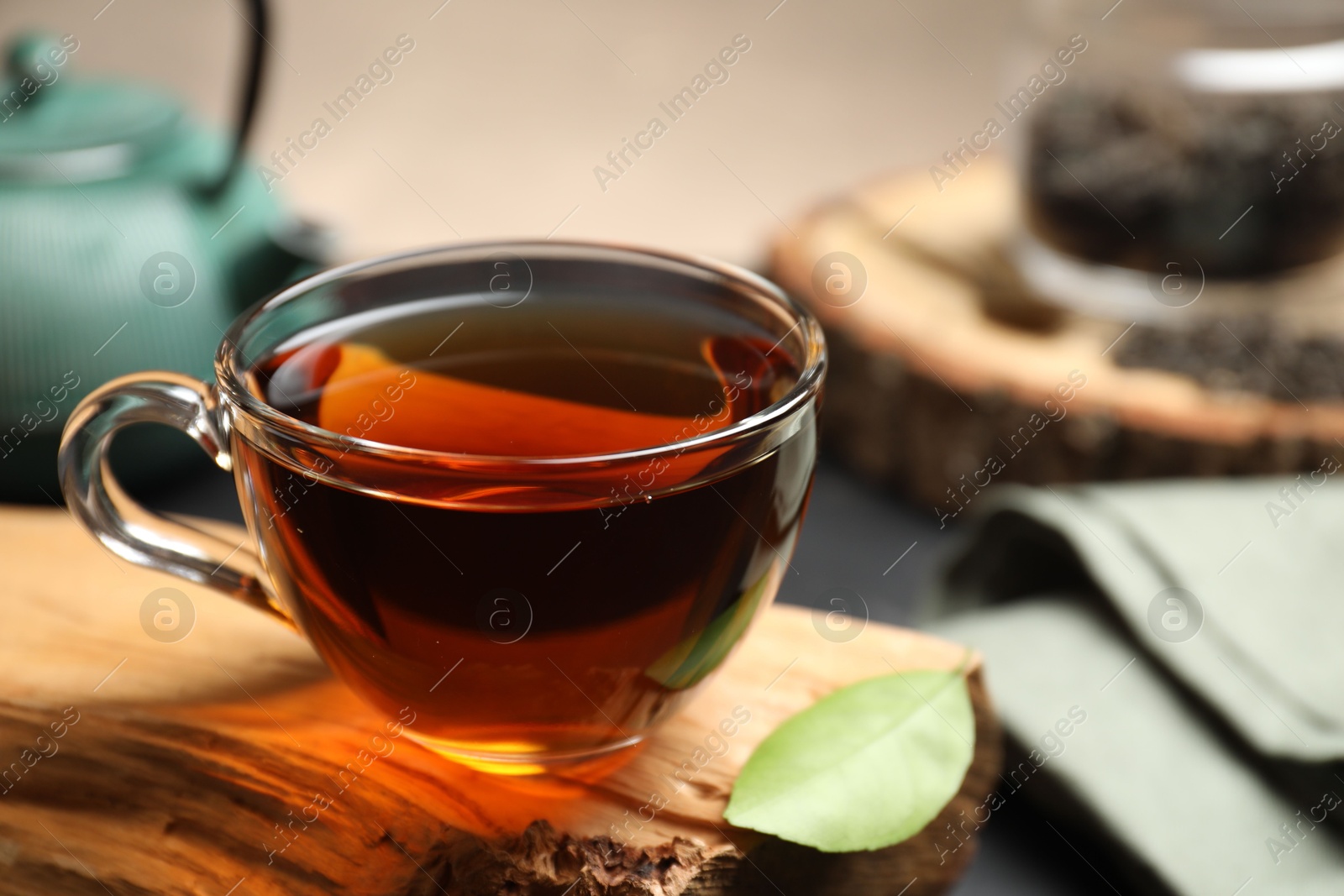 Photo of Aromatic black tea in cup and green leaf on wooden snag, closeup