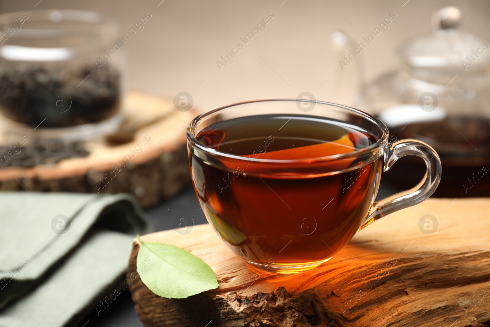 Photo of Aromatic black tea in cup and green leaf on wooden snag, closeup