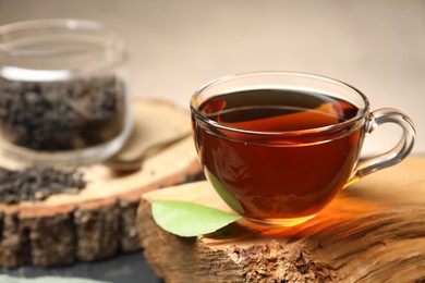 Photo of Aromatic black tea in cup and green leaf on wooden snag, closeup