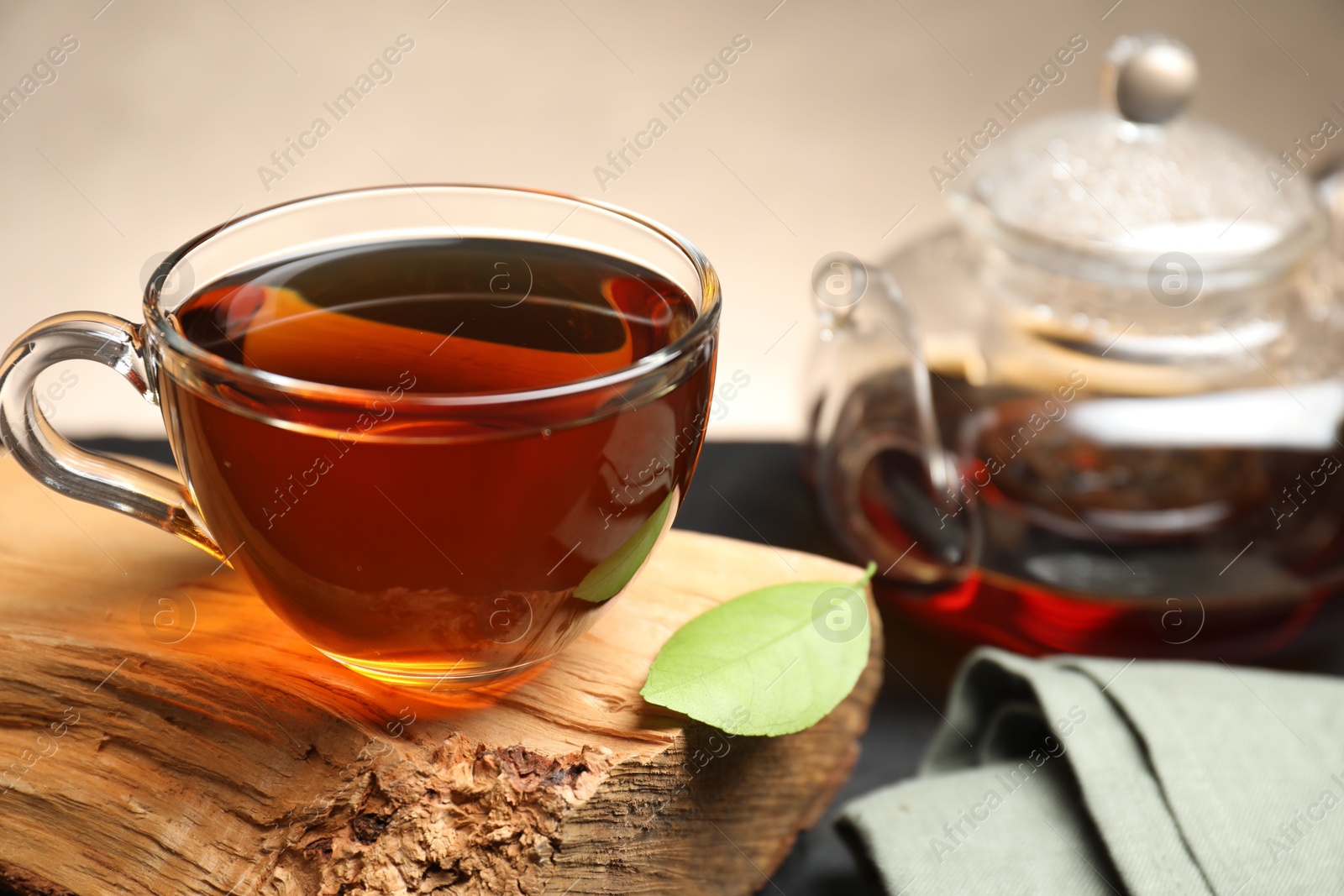 Photo of Aromatic black tea in cup and green leaf on table, closeup