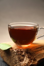 Photo of Aromatic black tea in cup and green leaf on wooden snag, closeup