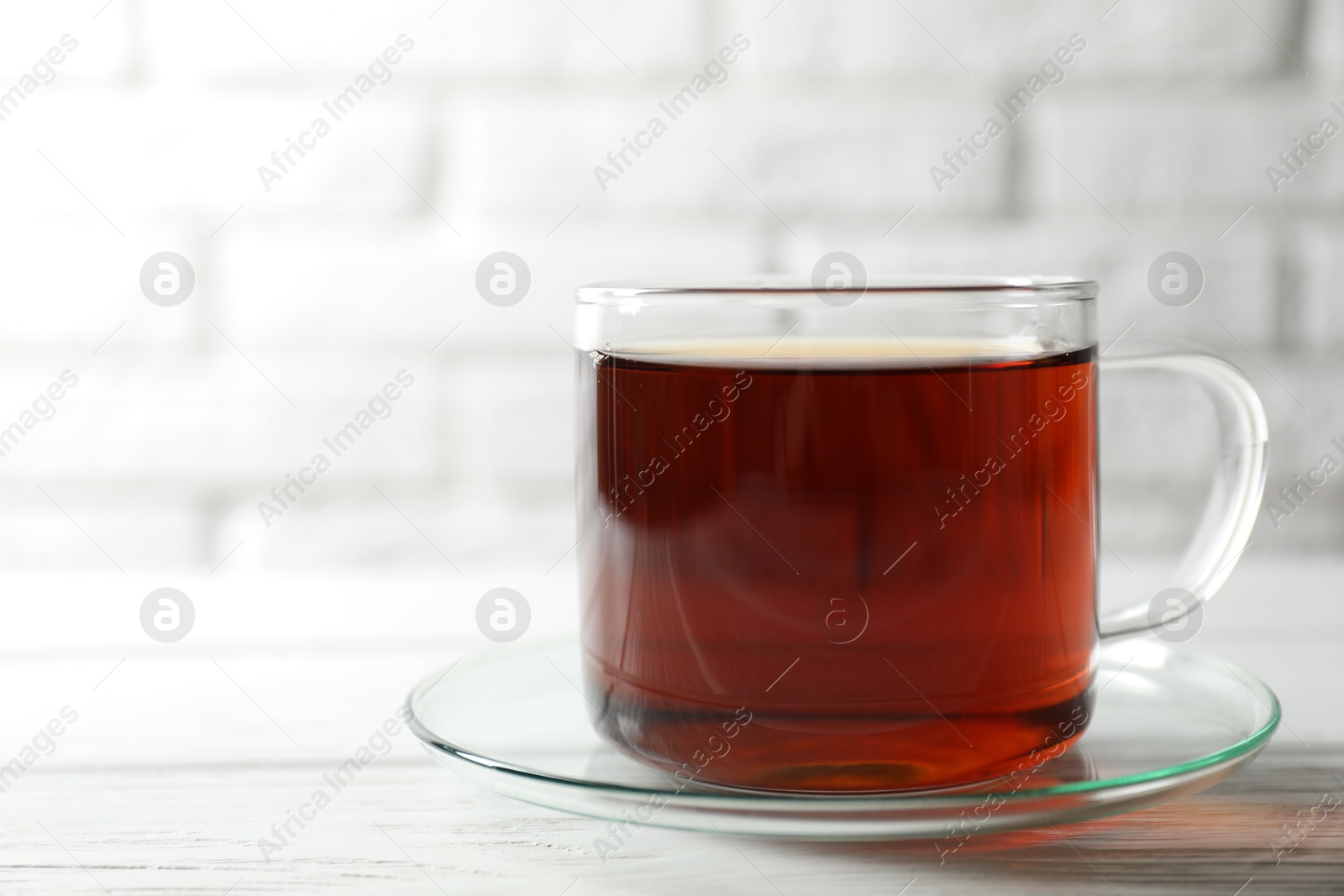 Photo of Aromatic black tea in cup on white wooden table, closeup. Space for text