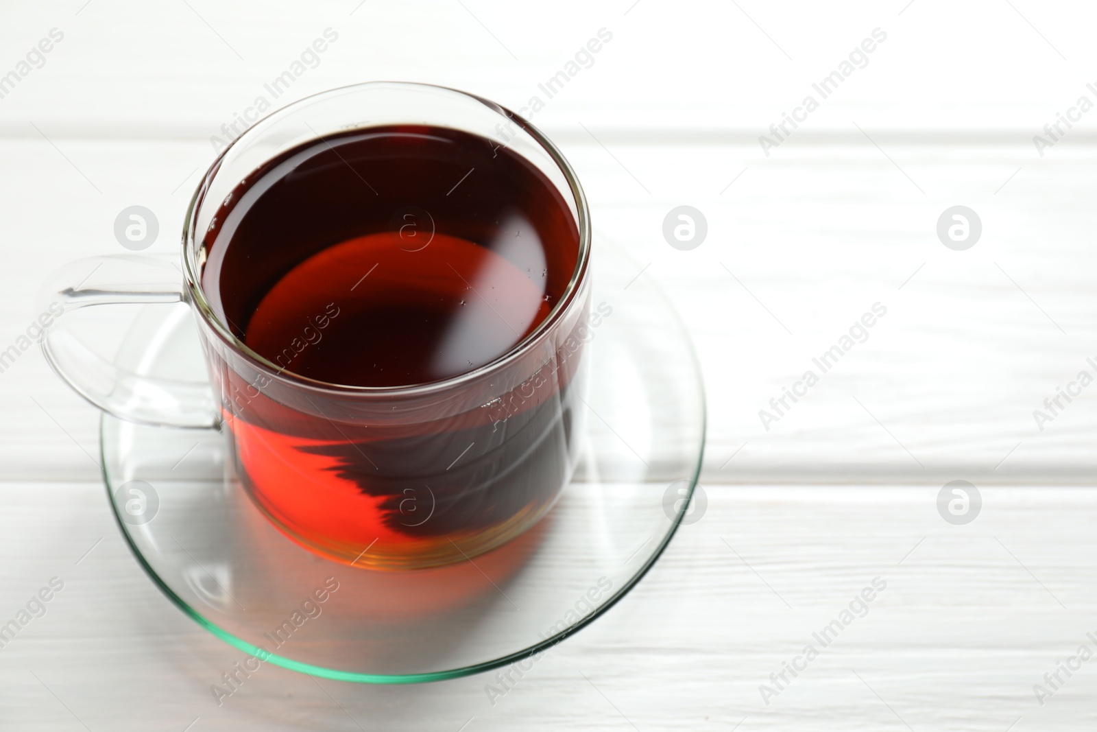 Photo of Aromatic black tea in cup on white wooden table, closeup. Space for text