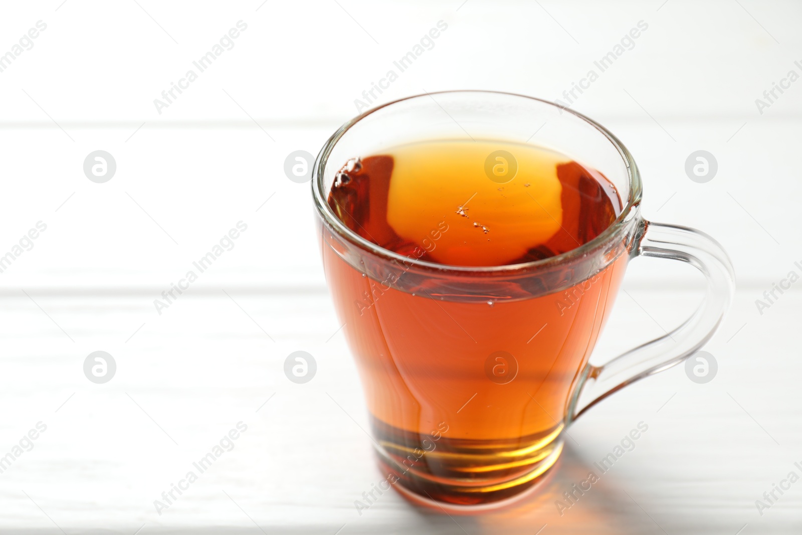 Photo of Aromatic black tea in cup on white wooden table, closeup. Space for text