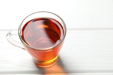 Photo of Aromatic black tea in cup on white wooden table, closeup. Space for text