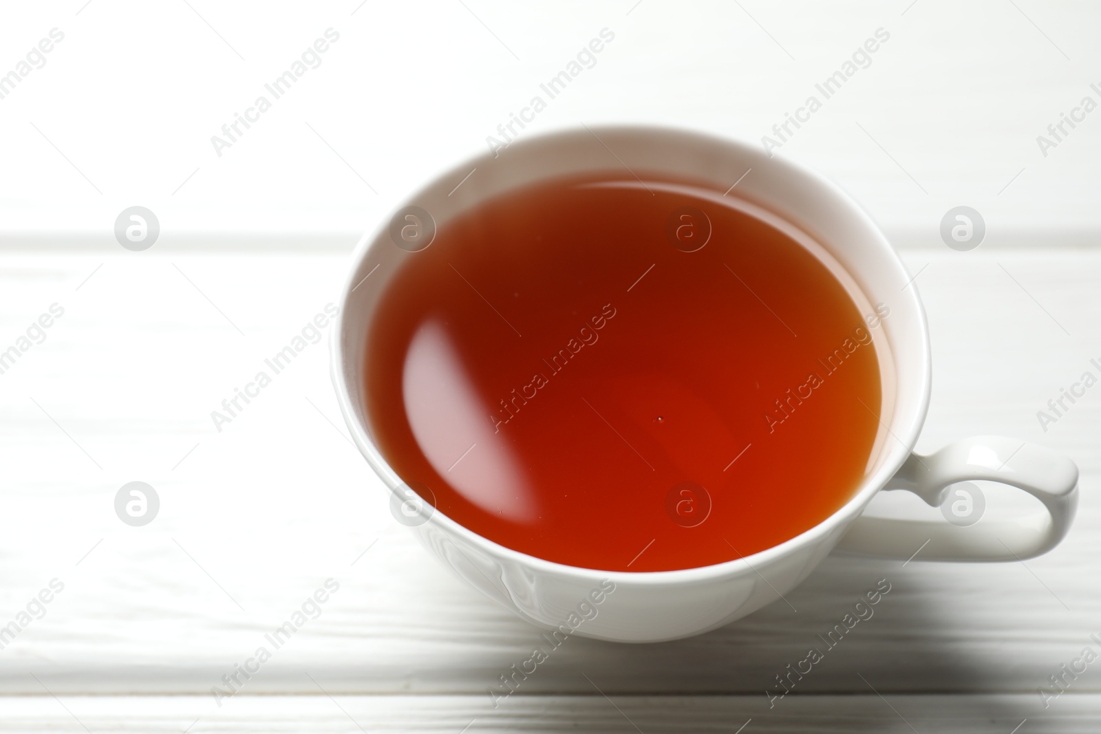 Photo of Aromatic black tea in cup on white wooden table, closeup