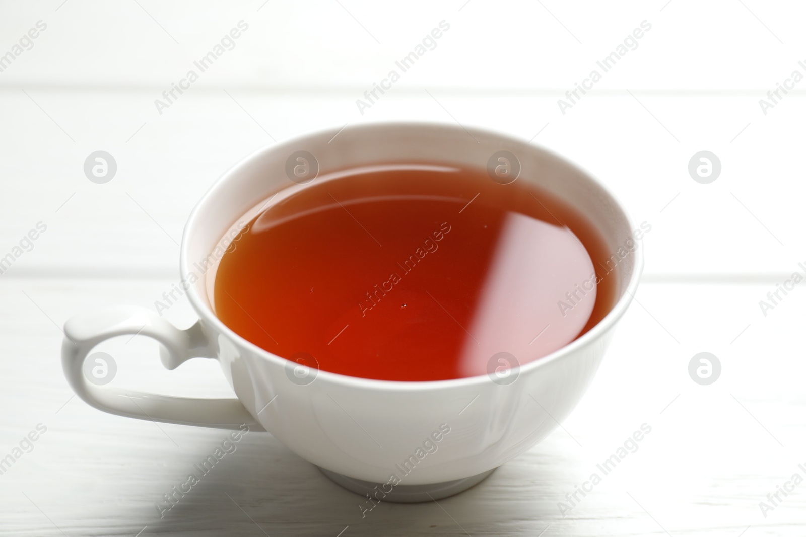 Photo of Aromatic black tea in cup on white wooden table, closeup