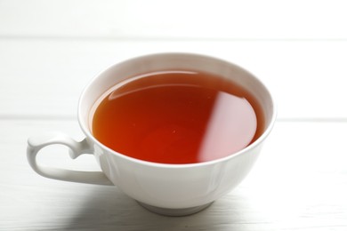 Photo of Aromatic black tea in cup on white wooden table, closeup