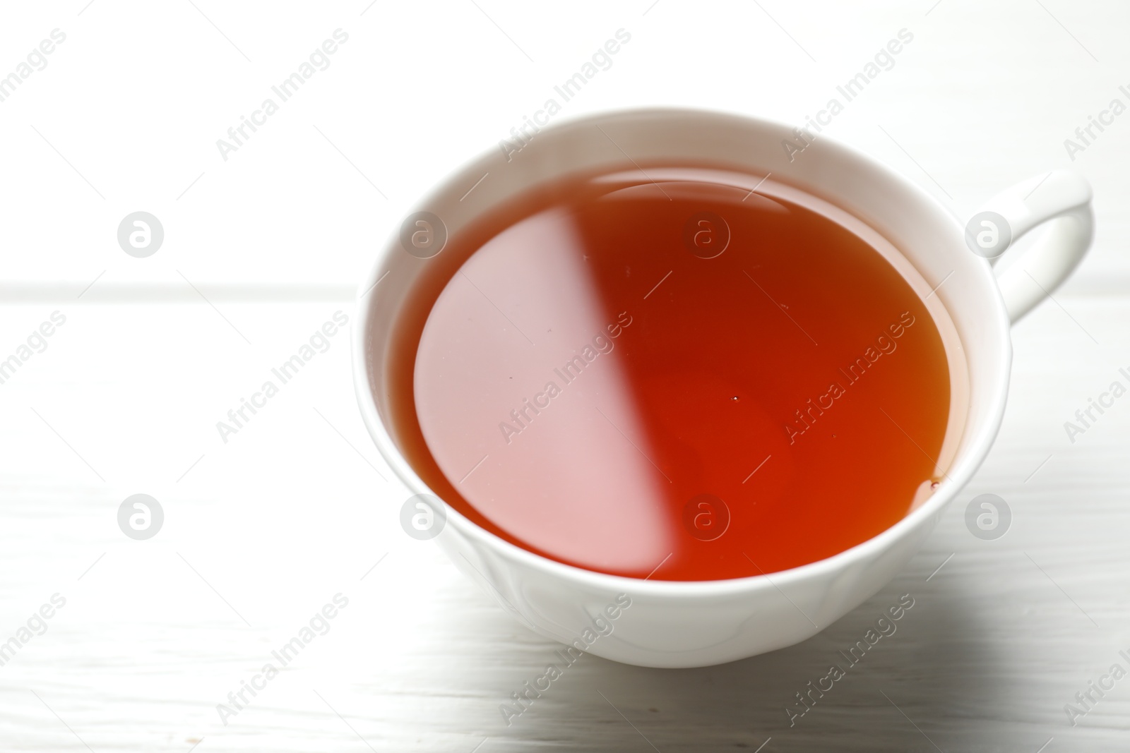 Photo of Aromatic black tea in cup on white wooden table, closeup. Space for text