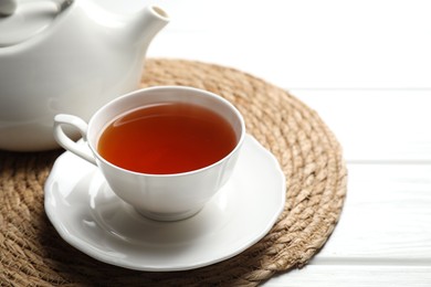 Photo of Aromatic black tea in cup and teapot on white wooden table, closeup