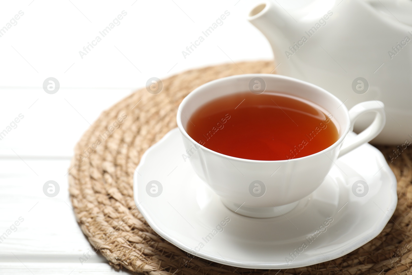 Photo of Aromatic black tea in cup and teapot on white wooden table, closeup