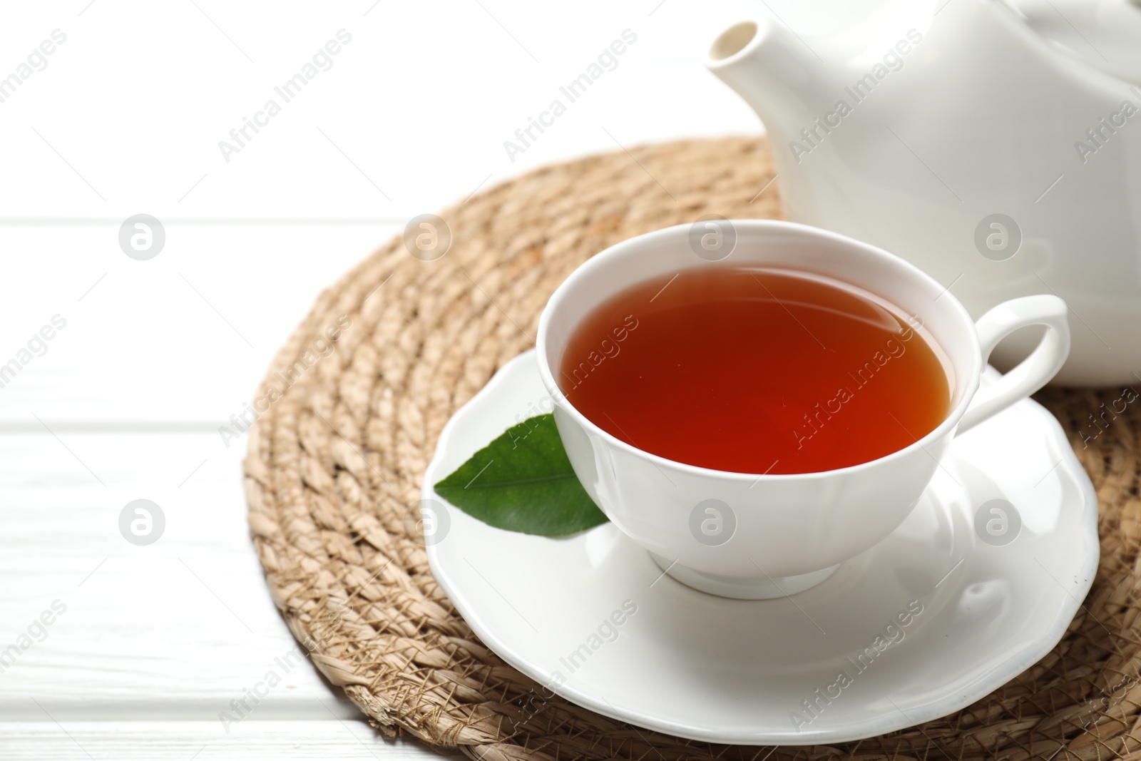 Photo of Aromatic black tea in cup and teapot on white wooden table, closeup