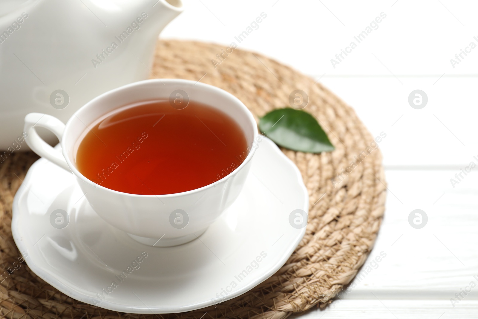 Photo of Aromatic black tea in cup and teapot on white wooden table, closeup