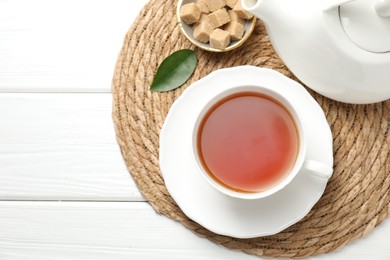 Photo of Aromatic black tea and brown sugar cubes on white wooden table, top view. Space for text