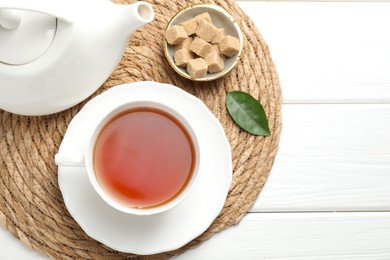 Photo of Aromatic black tea and brown sugar cubes on white wooden table, top view. Space for text