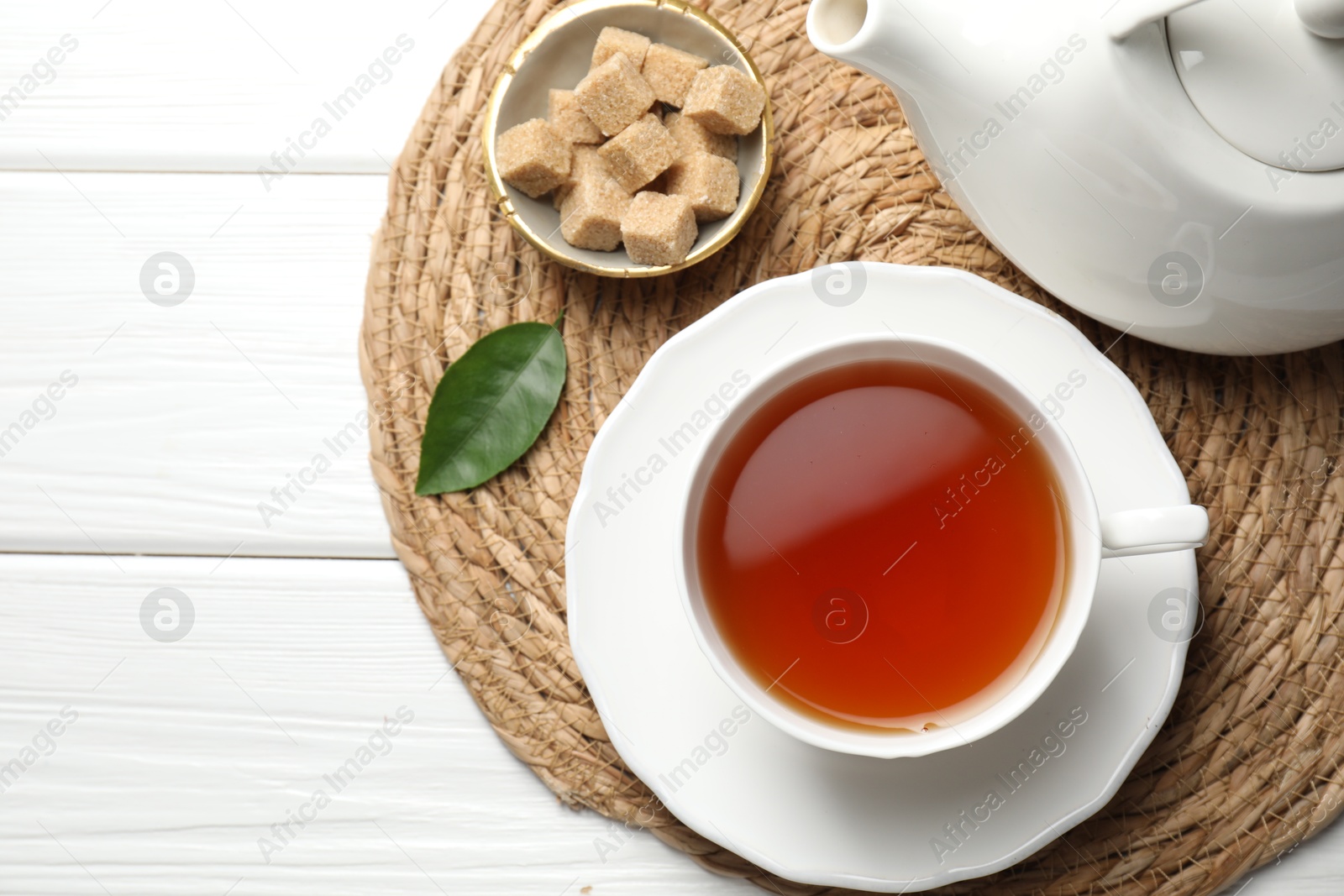 Photo of Aromatic black tea and brown sugar cubes on white wooden table, top view. Space for text