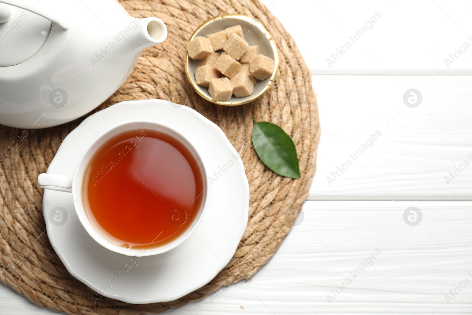 Photo of Aromatic black tea and brown sugar cubes on white wooden table, top view. Space for text