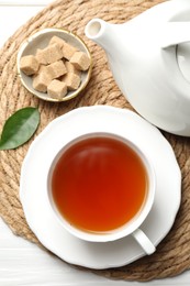 Photo of Aromatic black tea and brown sugar cubes on white wooden table, top view