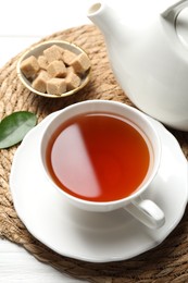 Photo of Aromatic black tea and brown sugar cubes on white wooden table, closeup