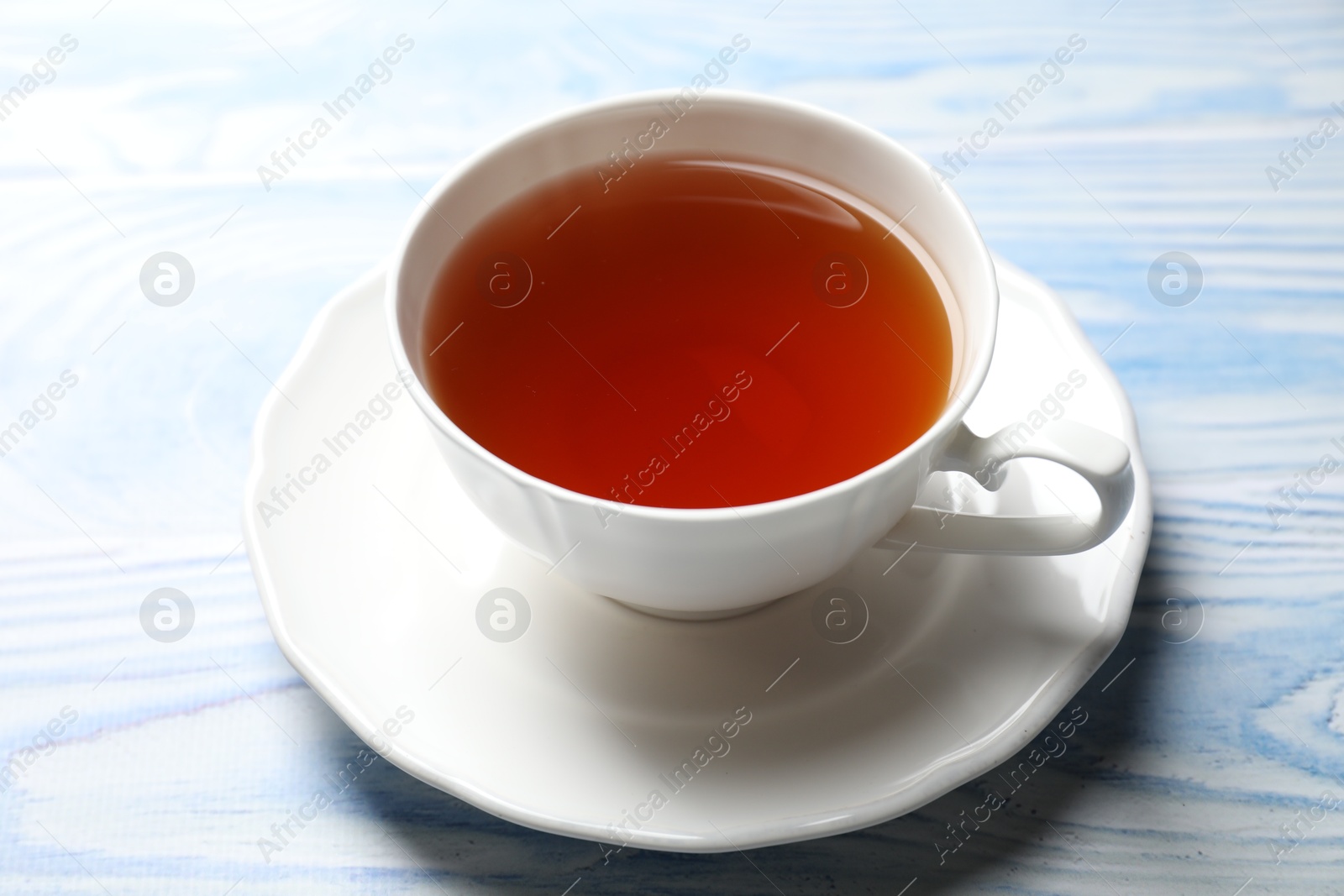 Photo of Aromatic black tea in cup on light blue wooden table, closeup