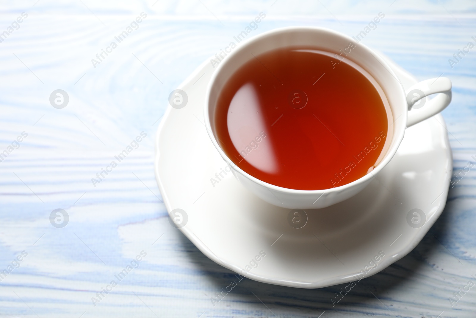 Photo of Aromatic black tea in cup on light blue wooden table, closeup. Space for text