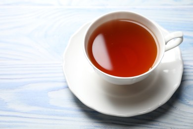 Photo of Aromatic black tea in cup on light blue wooden table, closeup. Space for text