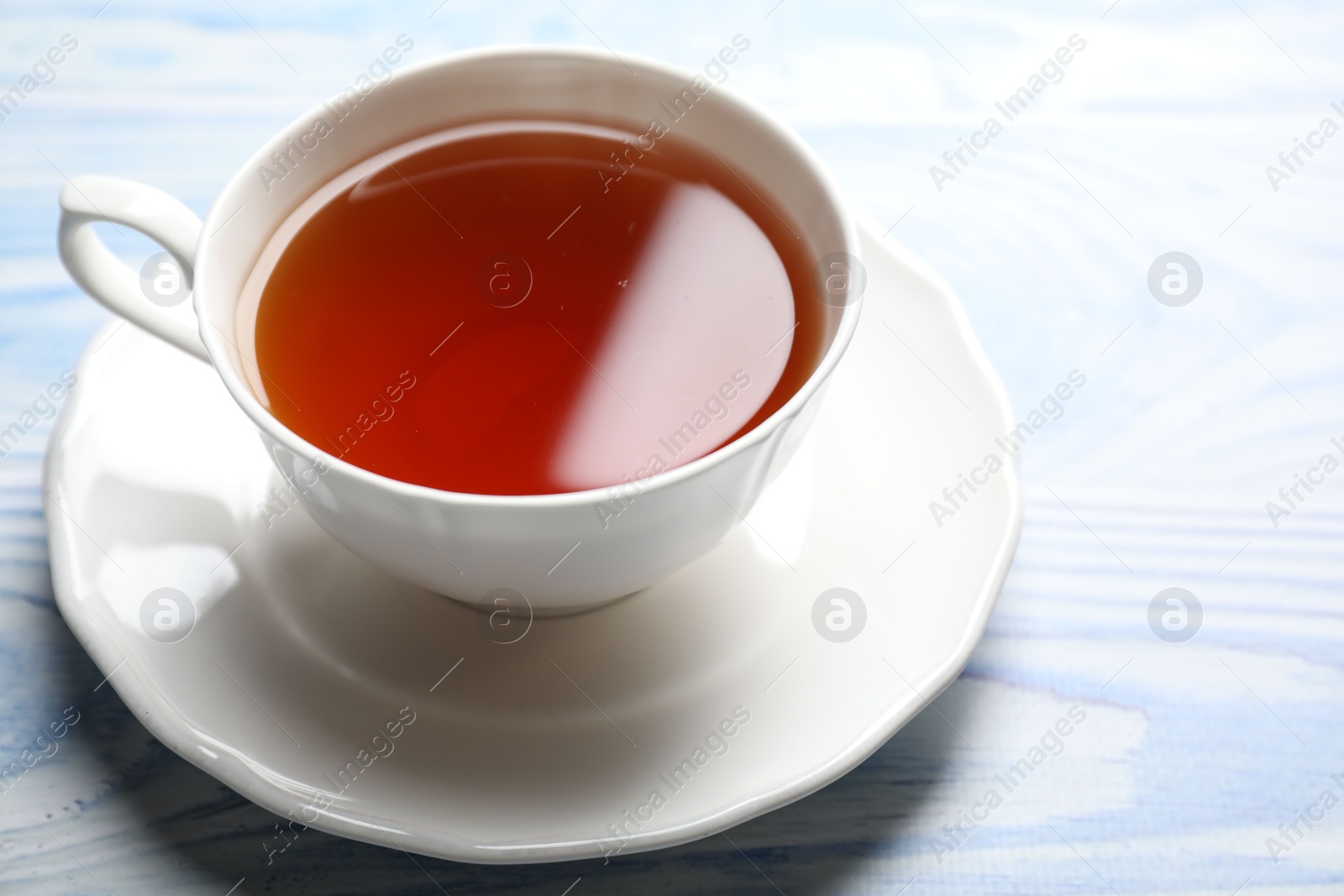 Photo of Aromatic black tea in cup on light blue wooden table, closeup