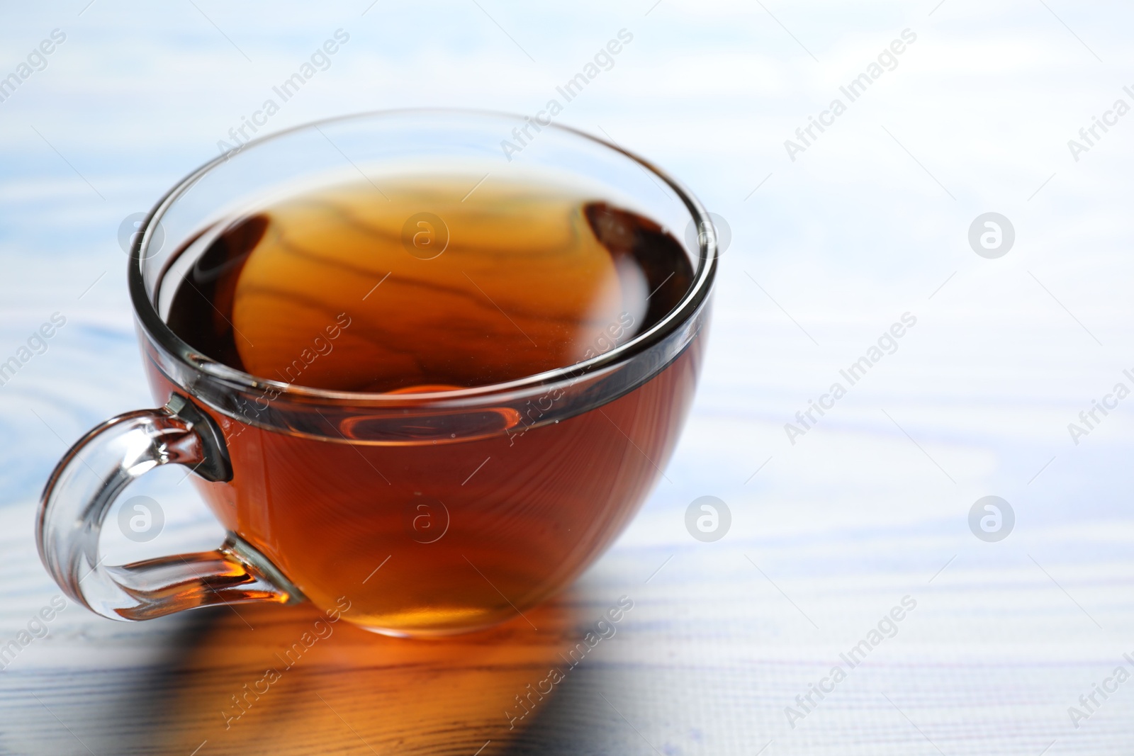 Photo of Aromatic black tea in cup on light blue wooden table, closeup. Space for text