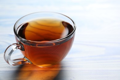 Aromatic black tea in cup on light blue wooden table, closeup. Space for text