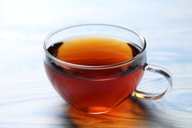 Aromatic black tea in cup on light blue wooden table, closeup