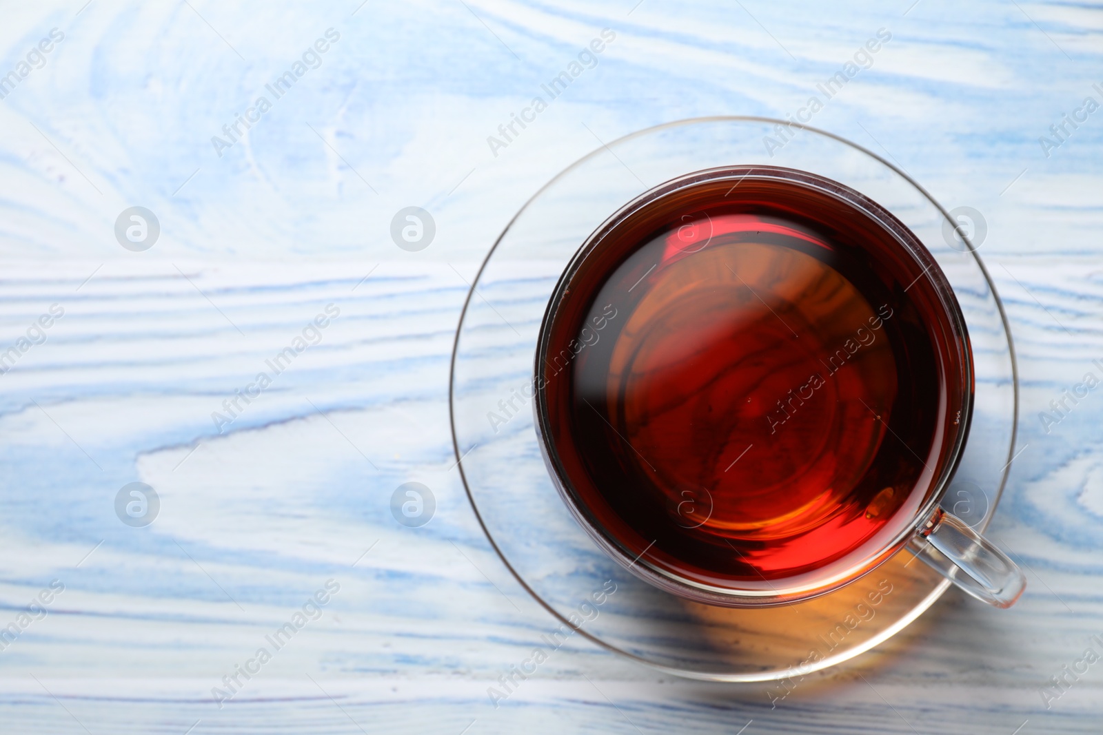 Photo of Aromatic black tea in cup on light blue wooden table, top view. Space for text