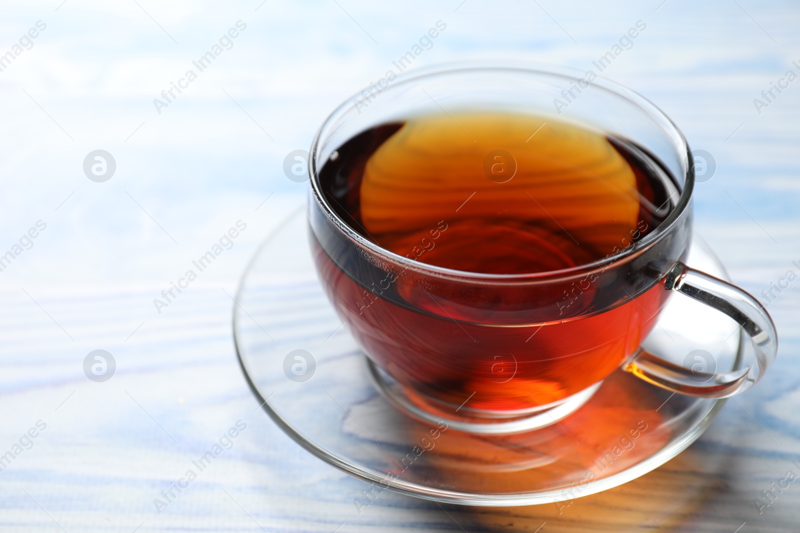 Photo of Aromatic black tea in cup on light blue wooden table, closeup. Space for text