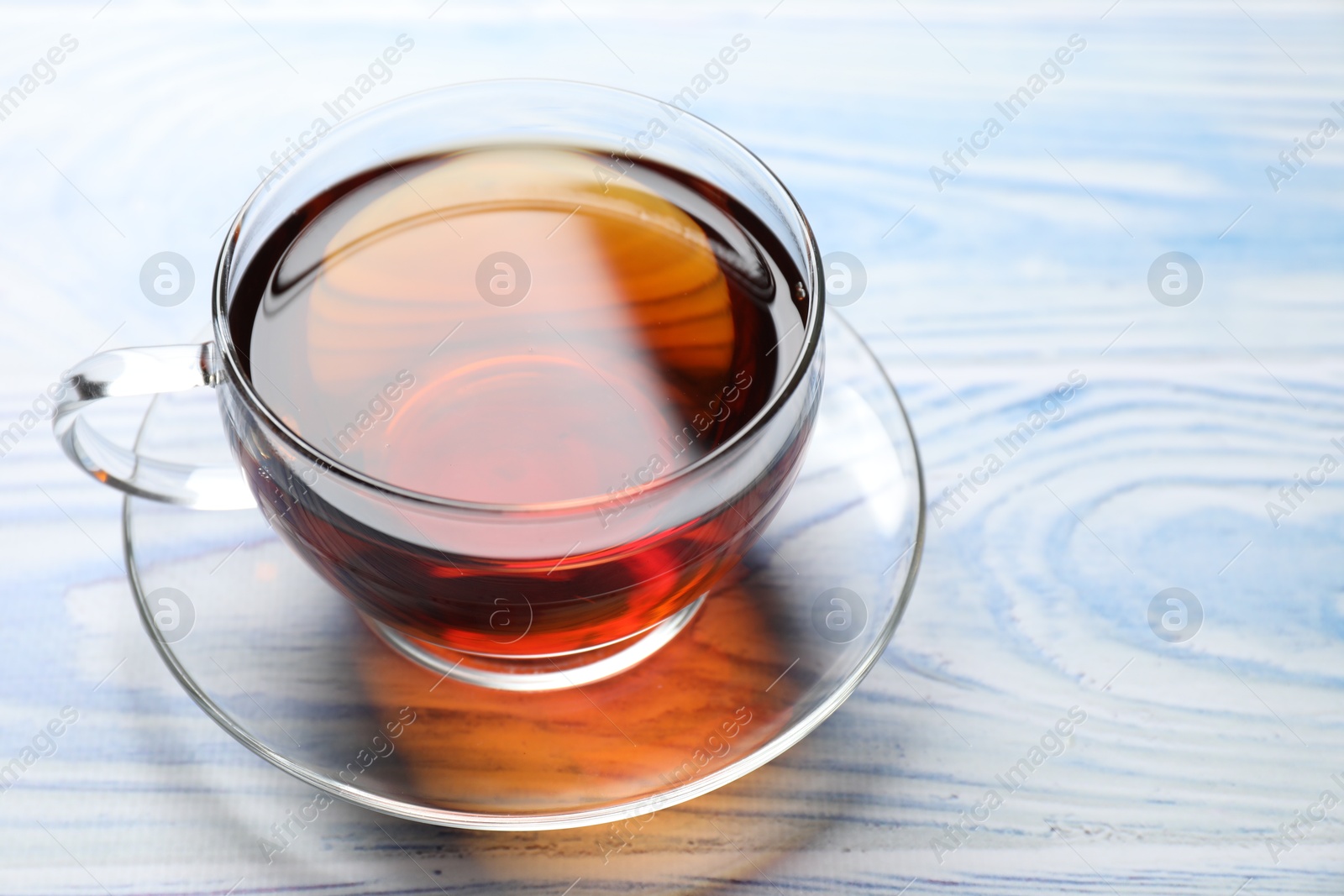 Photo of Aromatic black tea in cup on light blue wooden table, closeup. Space for text