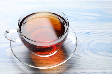 Photo of Aromatic black tea in cup on light blue wooden table, closeup. Space for text