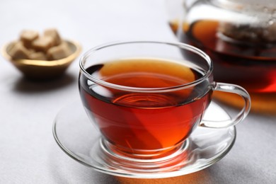 Photo of Aromatic black tea in cup and sugar on light table, closeup