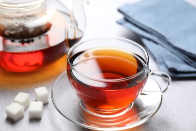 Photo of Aromatic black tea and sugar cubes on light table, closeup