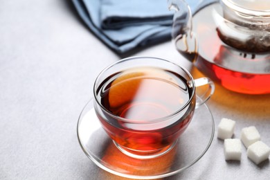 Photo of Aromatic black tea and sugar cubes on light table, closeup