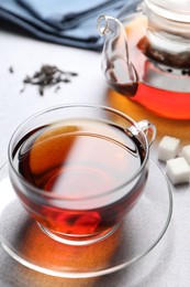 Photo of Aromatic black tea and sugar cubes on light table, closeup