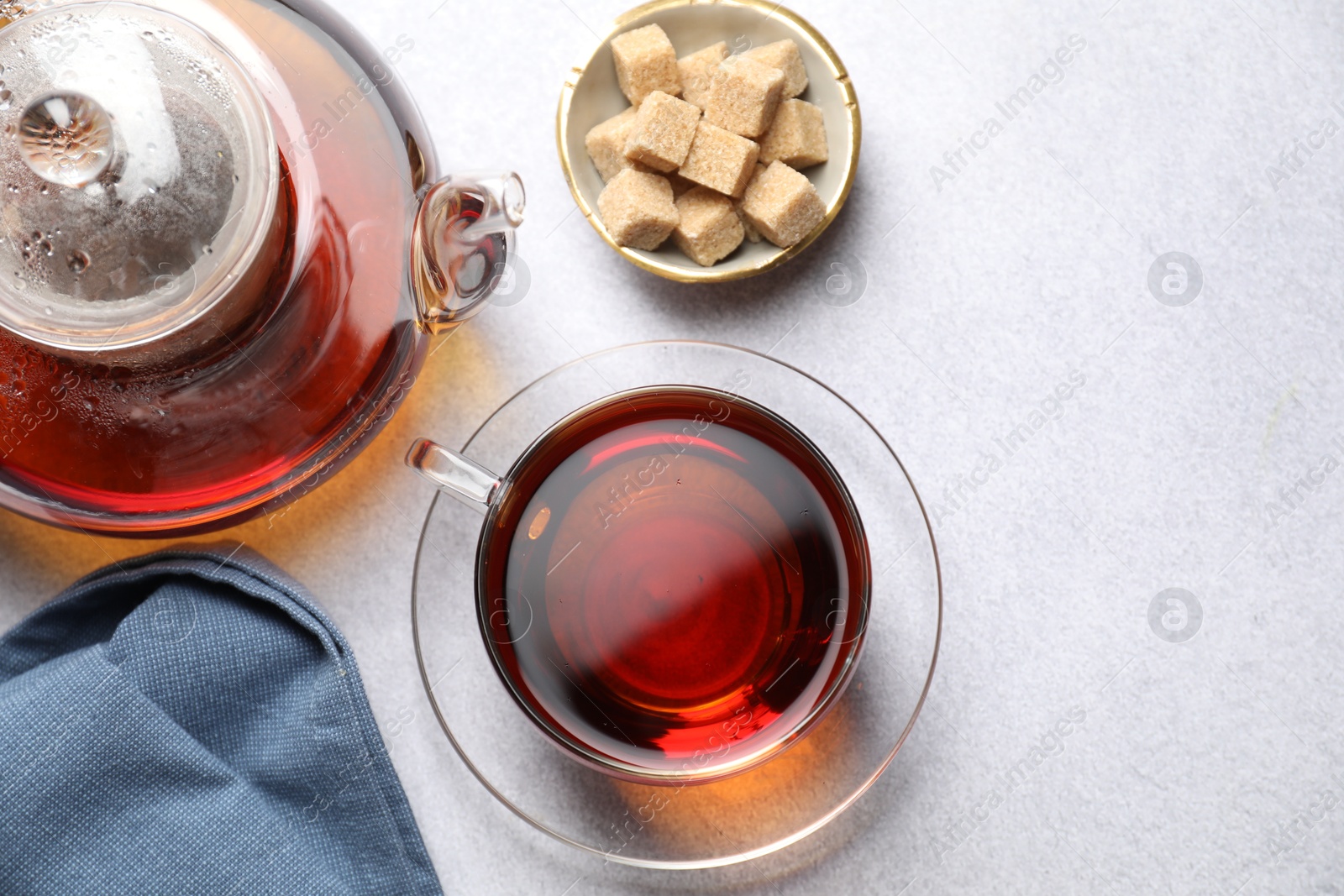 Photo of Aromatic black tea and brown sugar cubes on light table, flat lay