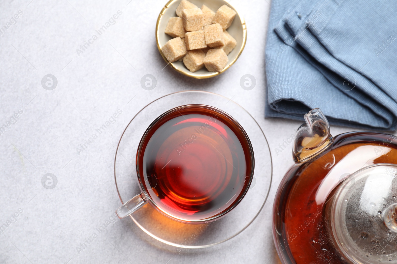 Photo of Aromatic black tea and brown sugar cubes on light table, flat lay