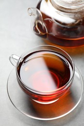 Photo of Aromatic black tea in cup and teapot on light table, closeup