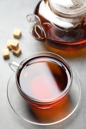 Photo of Aromatic black tea and brown sugar cubes on light grey table, closeup