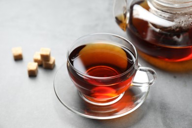 Photo of Aromatic black tea and brown sugar cubes on light grey table, closeup